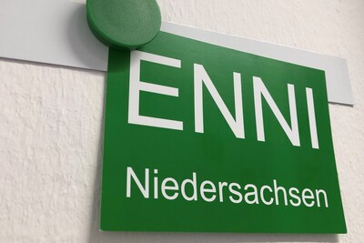 ENNI Logo - © Jutta Klaukien Grünes Schild mit der Aufschrift ENNI Niedersachsen, befestigt mit einem grünen Magneten an einer weißen Wand.