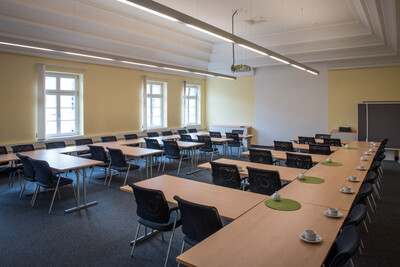 Kinosaal Oldenburg Mars-la-Tour-Straße - © Wolfgang Ehrecke Großer, leerer Konferenzraum mit U-förmiger Tischanordnung, schwarzen Stühlen, weißen Wänden und Fenstern an der linken Seite.
