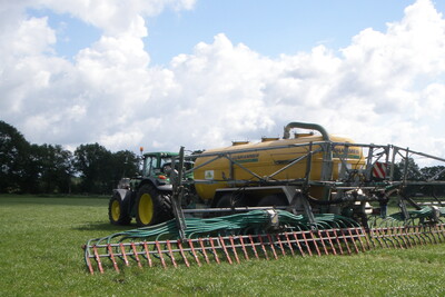 Traktor mit gro&szlig;em gelbem Tankanh&auml;nger und Verteiler auf einem gr&uuml;nen Feld unter bew&ouml;lktem Himmel.